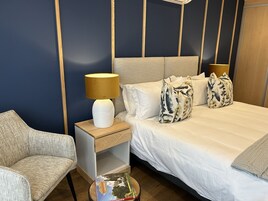 Una habitación de hotel con cama, mesita de noche, lámpara, silla y un libro en el suelo.