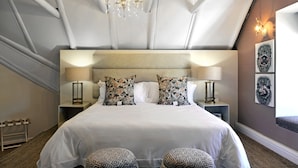 A hotel room with a large bed, two bedside tables with lamps, a chandelier, and a wall-mounted artwork. - Mirabelle Guesthouse (Franschhoek)