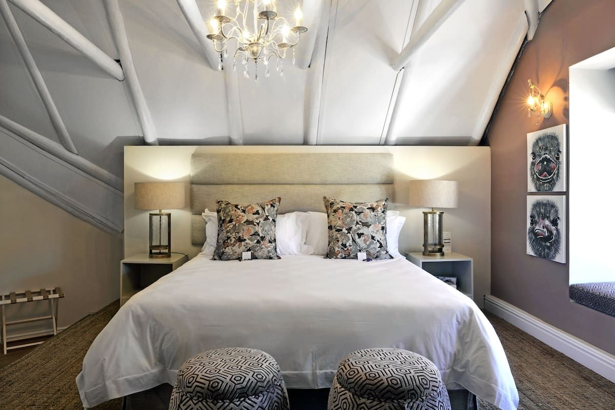 A hotel room with a large bed, two bedside tables with lamps, a chandelier, and a wall-mounted artwork.