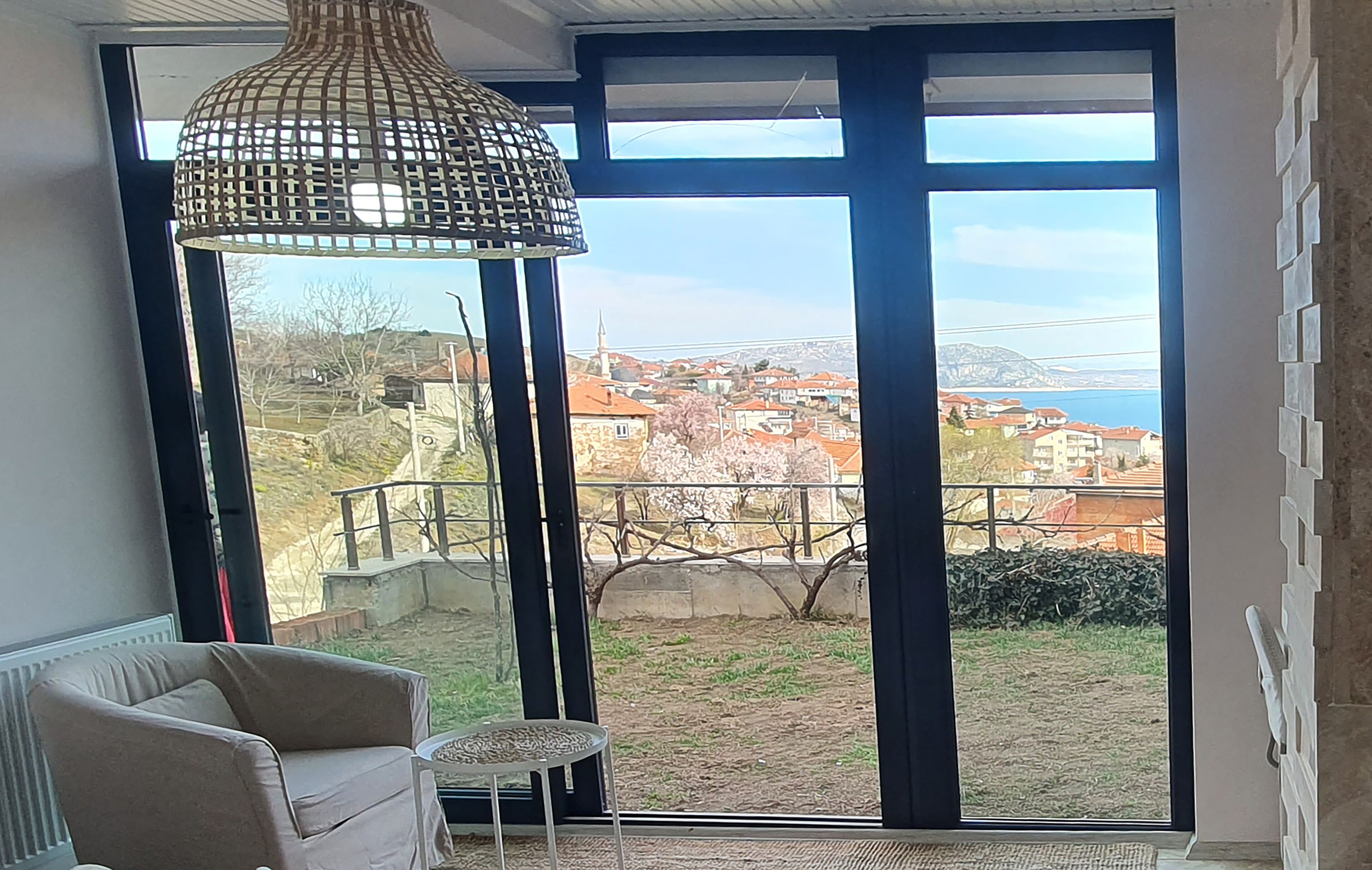 A room with large windows, a wicker lamp, a chair, and a small table.