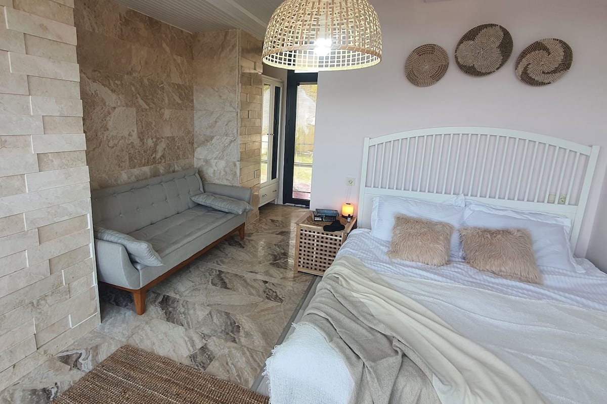 A bedroom with a stone wall, a sofa, a bed with white headboard, and a hanging light fixture.