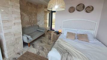 A bedroom with a stone wall, a sofa, a bed with white headboard, and a hanging light fixture.