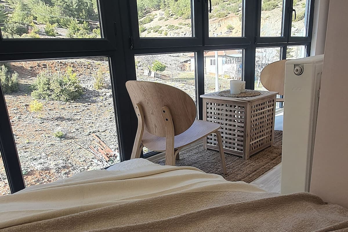 A room with large windows, a wooden chair, a small table, and a bed.