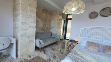 A room with a stone wall, a grey sofa, a white bed, and a desk with a chair.