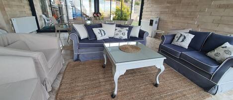 Un espacio exterior moderno con un conjunto de sofás azules, una mesa de centro de vidrio y una alfombra tejida.