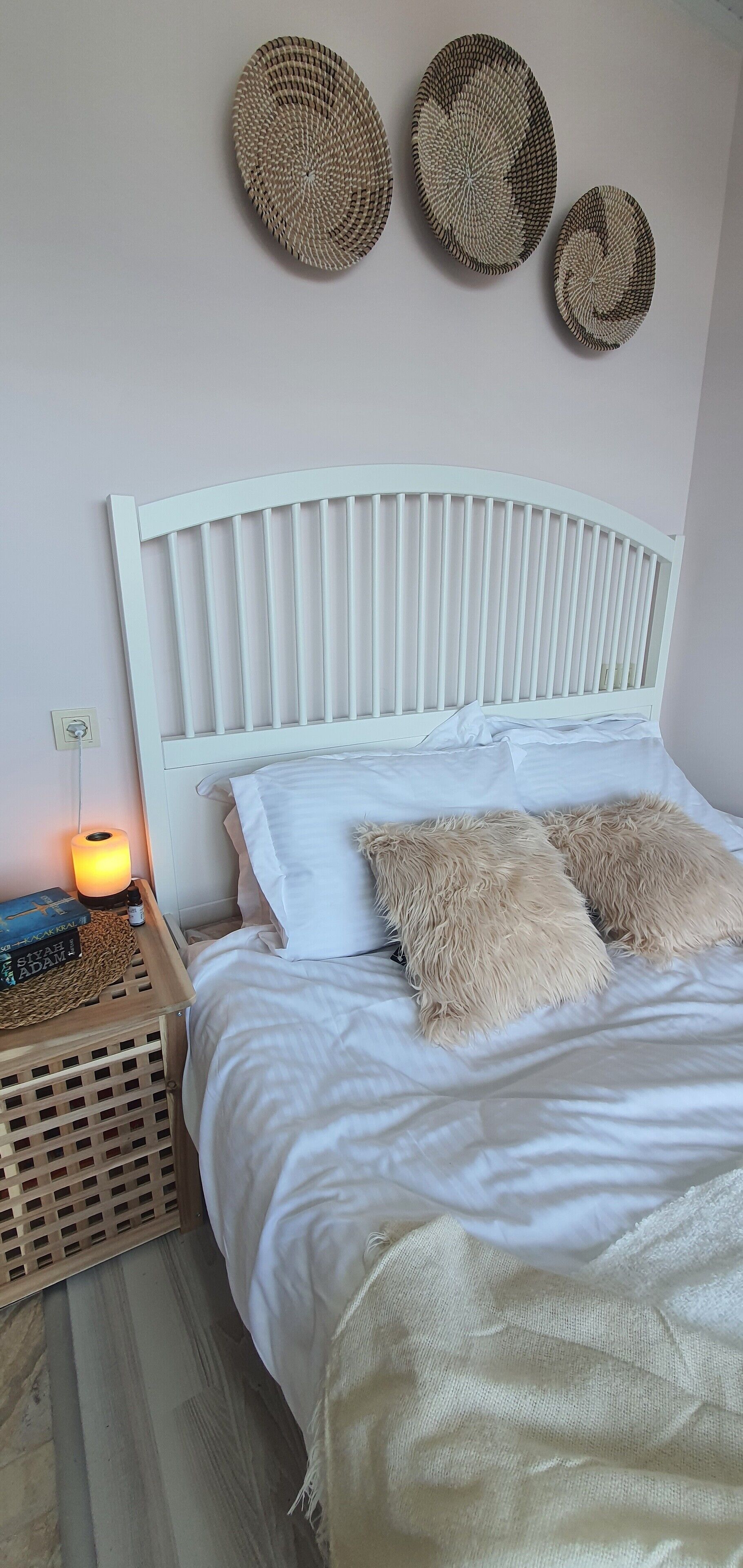Un lit avec une tête de lit blanche, deux oreillers moelleux et une table de chevet avec une lampe et des livres.