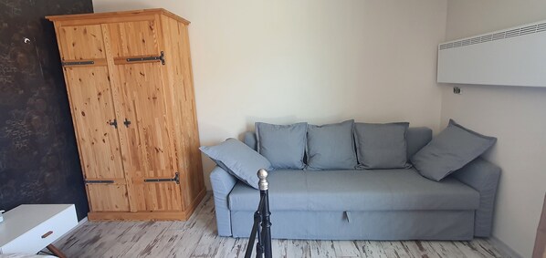 A room with a grey sofa, a wooden wardrobe, and a tripod.