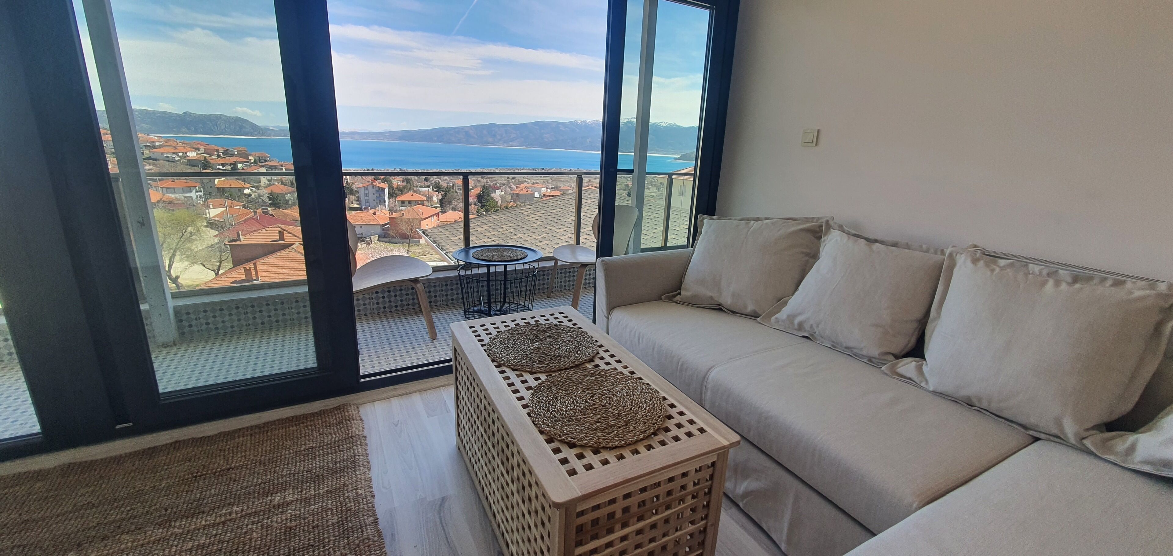 Un balcón con vistas a un pueblo costero, un sofá y una mesita con un mantel tejido.