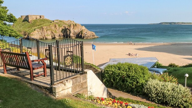 A coastal view with a beach, a historic fort, and a garden with a bench. - Bwthyn Canol (Haverfordwest)