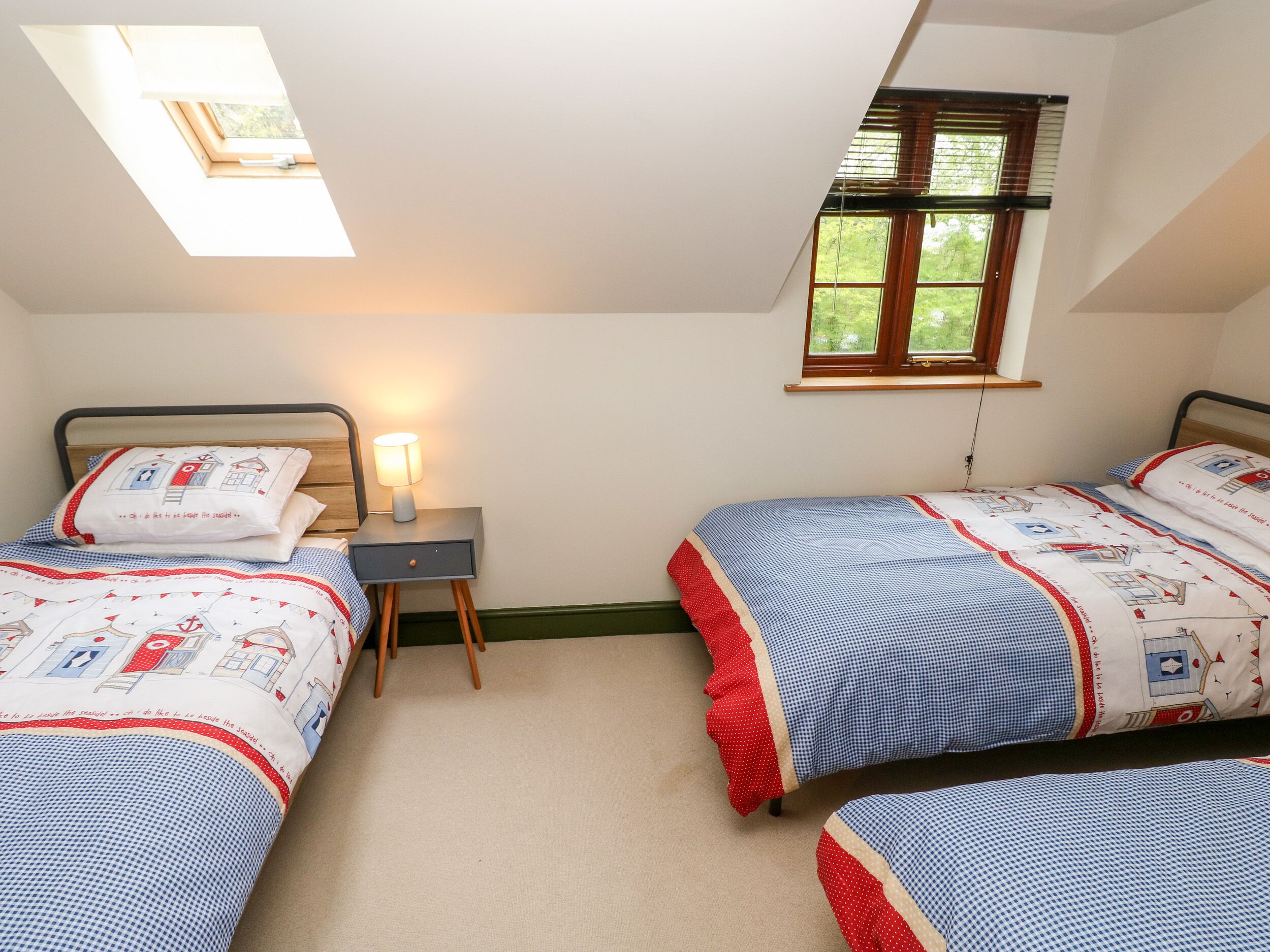 A bedroom with two beds, a nightstand, a lamp, and a skylight.