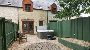 A patio with a wooden table and benches, a hot tub, and a green fence. - Bwthyn Canol (Haverfordwest)