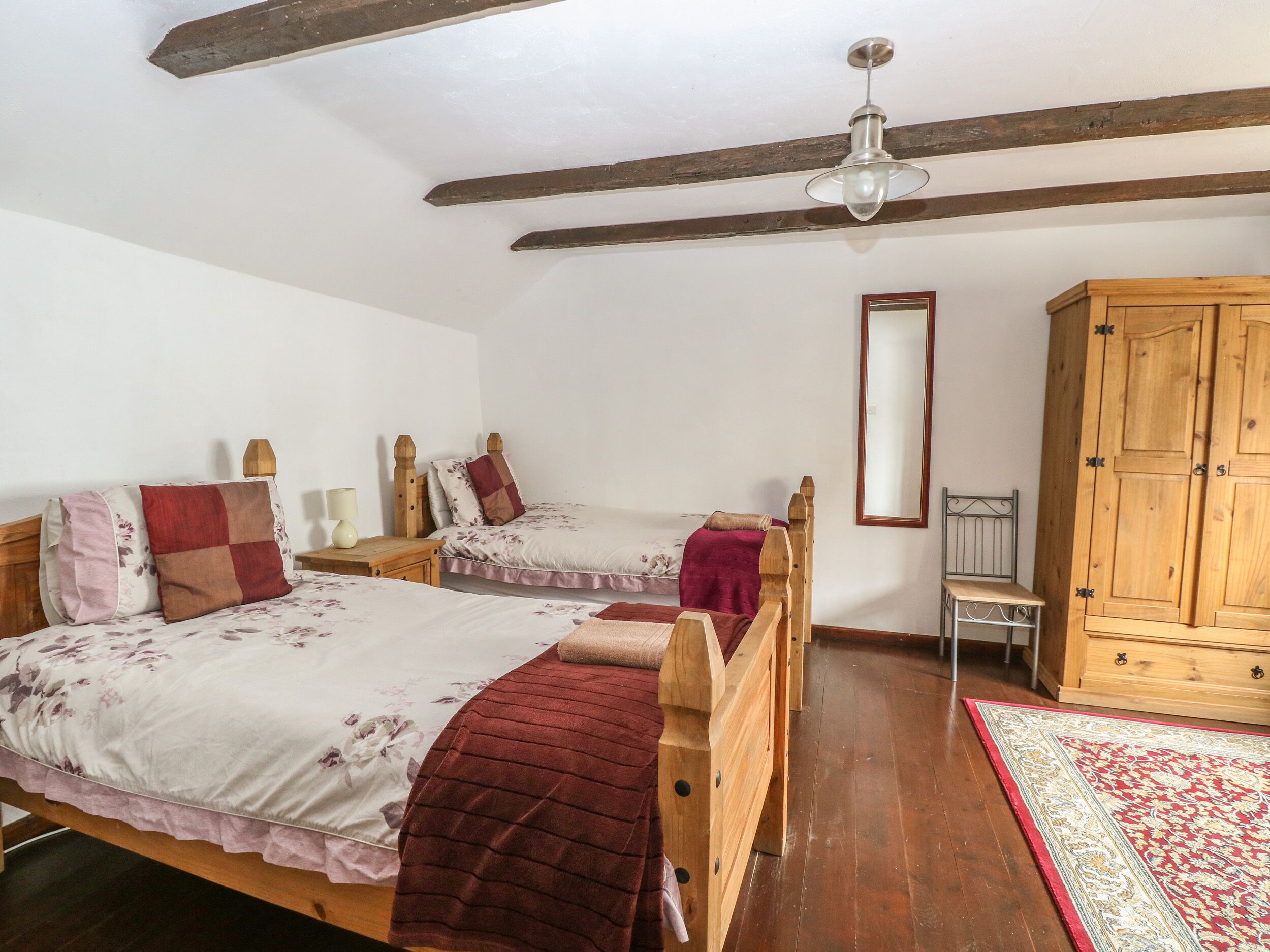A bedroom with two wooden beds, a wooden wardrobe, a mirror, and a ceiling fan.