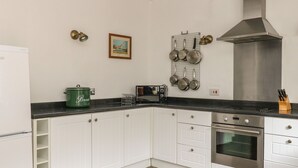 A modern kitchen with white cabinets, a black countertop, a stainless steel range hood, and a built-in oven. - The Old Barn (Norwich)