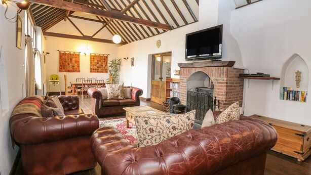 A living room with leather sofas, a fireplace, and a television. - The Old Barn (Norwich)