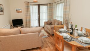 A living room with a sofa, a dining table set for two, and a television. - 2 Chandlers Yard (Burry Port)