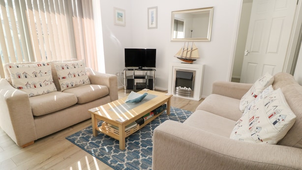 Un salon avec deux canapés beige, une table basse en bois, un téléviseur à écran plat, une cheminée et un grand miroir au mur.