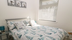 Un lit bien fait, avec une couette aux motifs marins, une lampe de chevet et une petite table sur laquelle se trouve une télécommande.