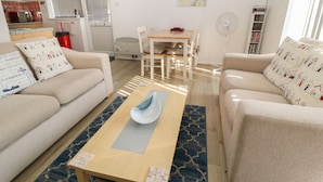 Un salon moderne avec deux canapés beige, une table basse en bois et un coin repas comprenant une table et des chaises blanches.