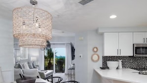 Una cocina moderna con muebles blancos, horno integrado y comedor con mesa y sillas blancas.