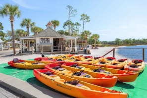 Kayaks alineados en un muelle, con un edificio pequeño al fondo.