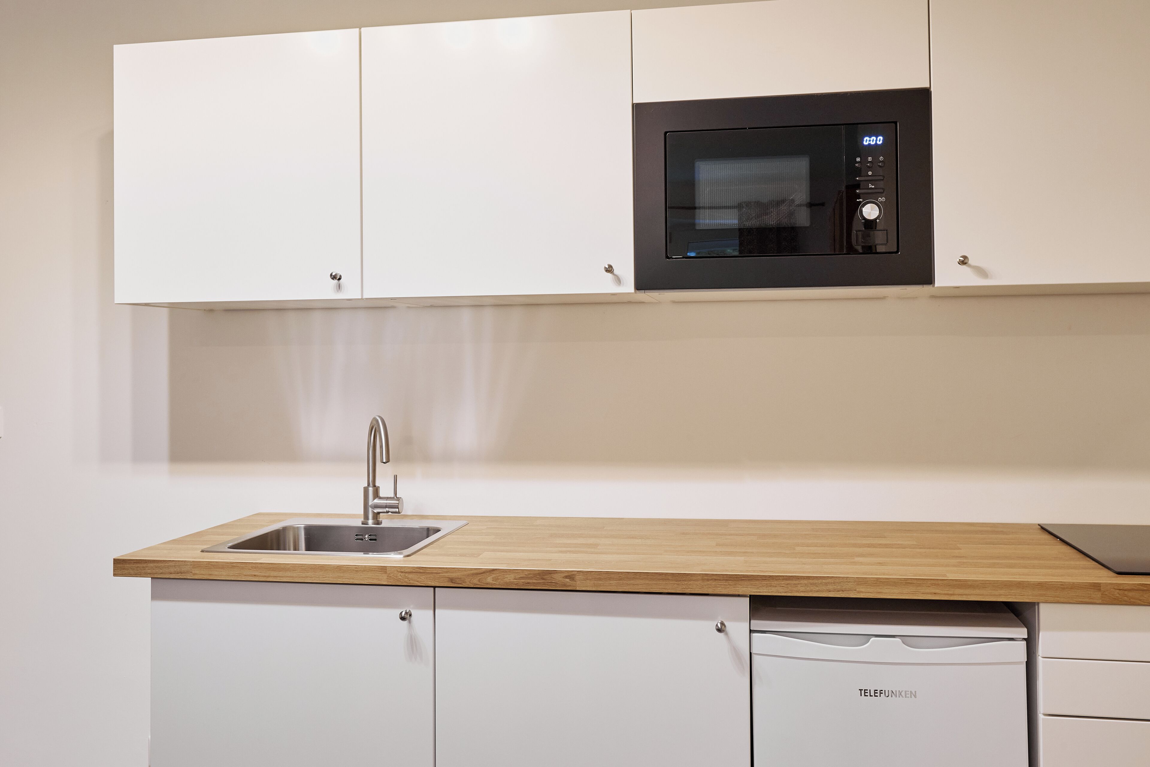 Een moderne keuken met witte kasten, een ingebouwde magnetron, een spoelbak en een vaatwasser.