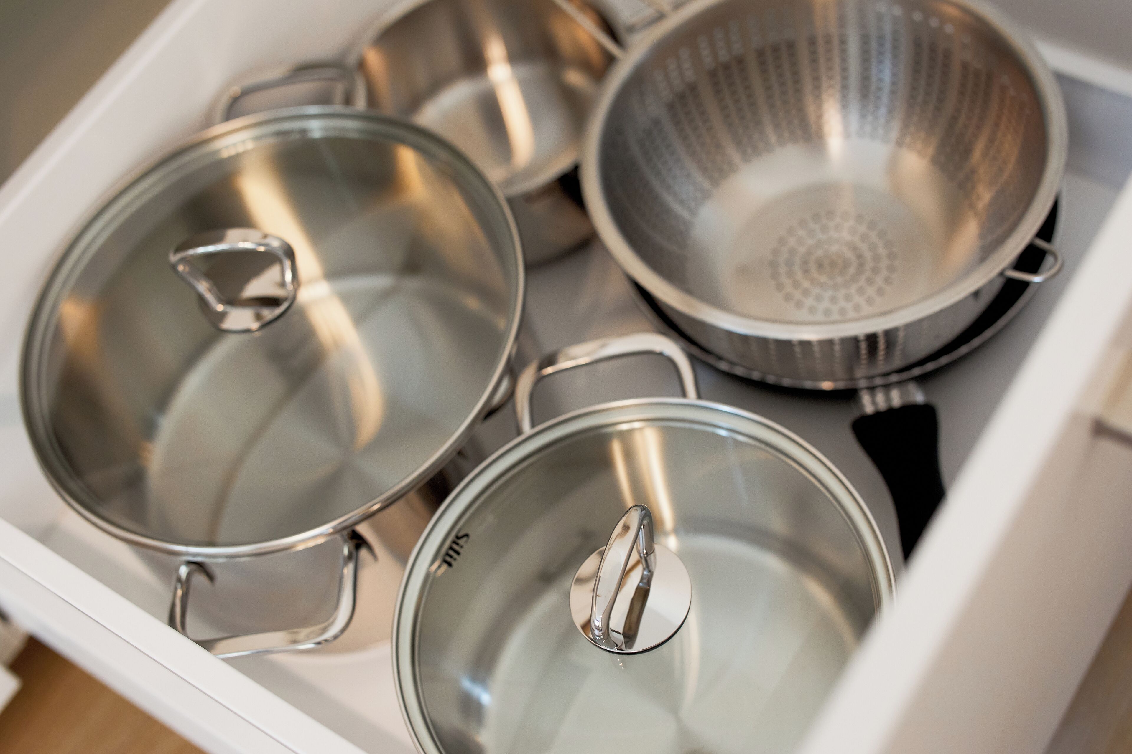 A kitchen drawer with stainless steel pots and pans.