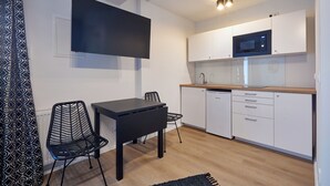 A modern kitchen with white cabinets, a microwave, and a black dining table with chairs. - Humboldt41 (Nuremberg)