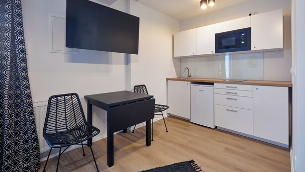 A modern kitchen with white cabinets, a microwave, and a black dining table with chairs. - Humboldt41 (Nuremberg)
