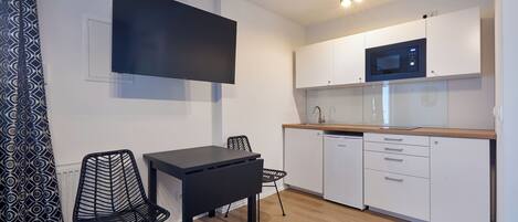 A modern kitchen with white cabinets, a microwave, and a black dining table with chairs.