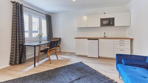 A compact living space with a kitchenette, a dining area with a table and chairs, and a blue sofa. - Humboldt41 (Nuremberg)