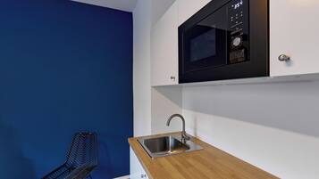 Una cocina compacta con microondas integrado, un lavamanos de acero inoxidable y una silla moderna.