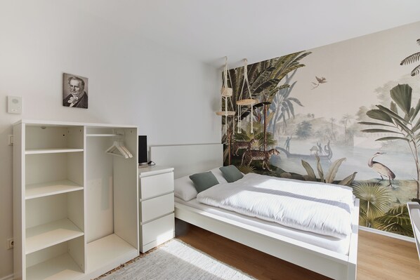 A modern bedroom with a bed, a wardrobe, and a mural of a tropical scene.