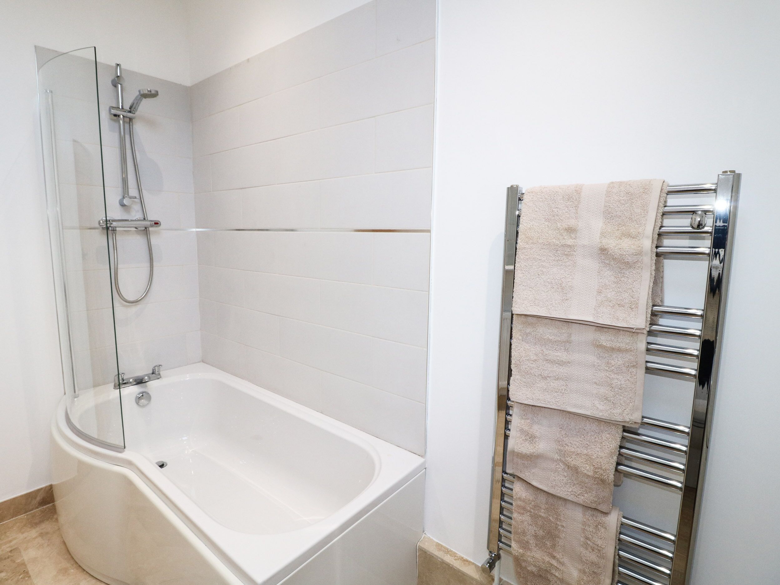 A modern bathroom with a glass-enclosed shower, a white bathtub, and a towel rack with multiple towels.