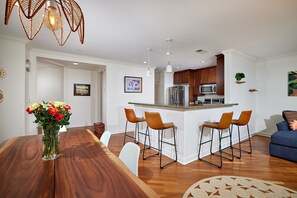 A modern kitchen with a central island, bar stools, and a dining table with a vase of flowers. - May discounted Ocean View with AC (Oceanside)