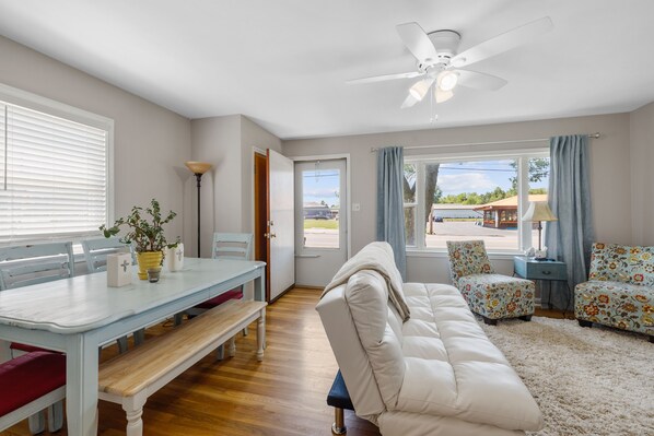 A spacious living room with a white sofa, a dining table with chairs, and a ceiling fan.