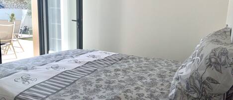 A bedroom with a bed covered in floral-patterned bedding, a bedside lamp, and a view of the outside through an open door.