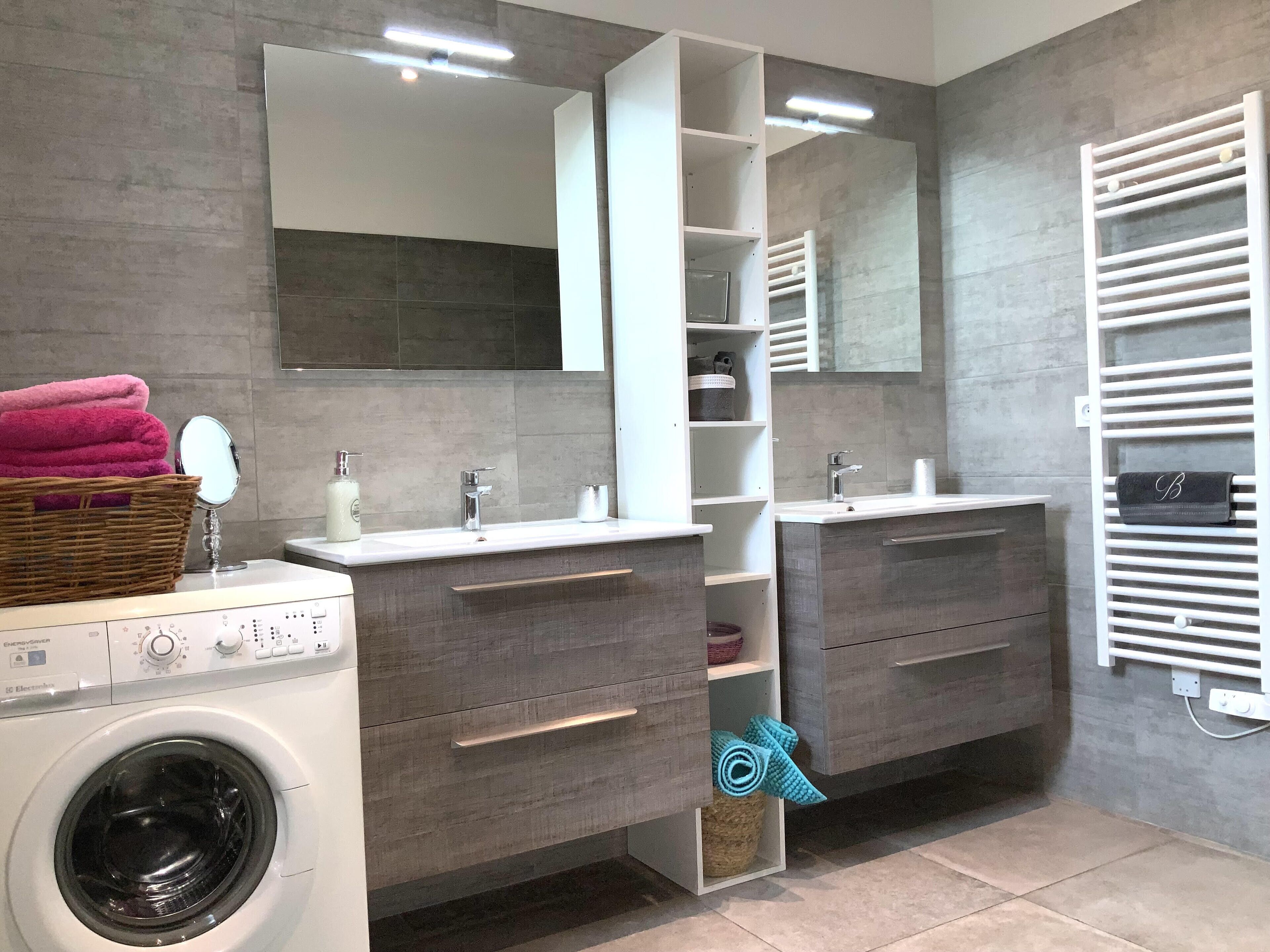 Une salle de bain moderne dotée de deux lavabos, d’un miroir encastré, d’un lave-linge et d’un porte-serviettes.