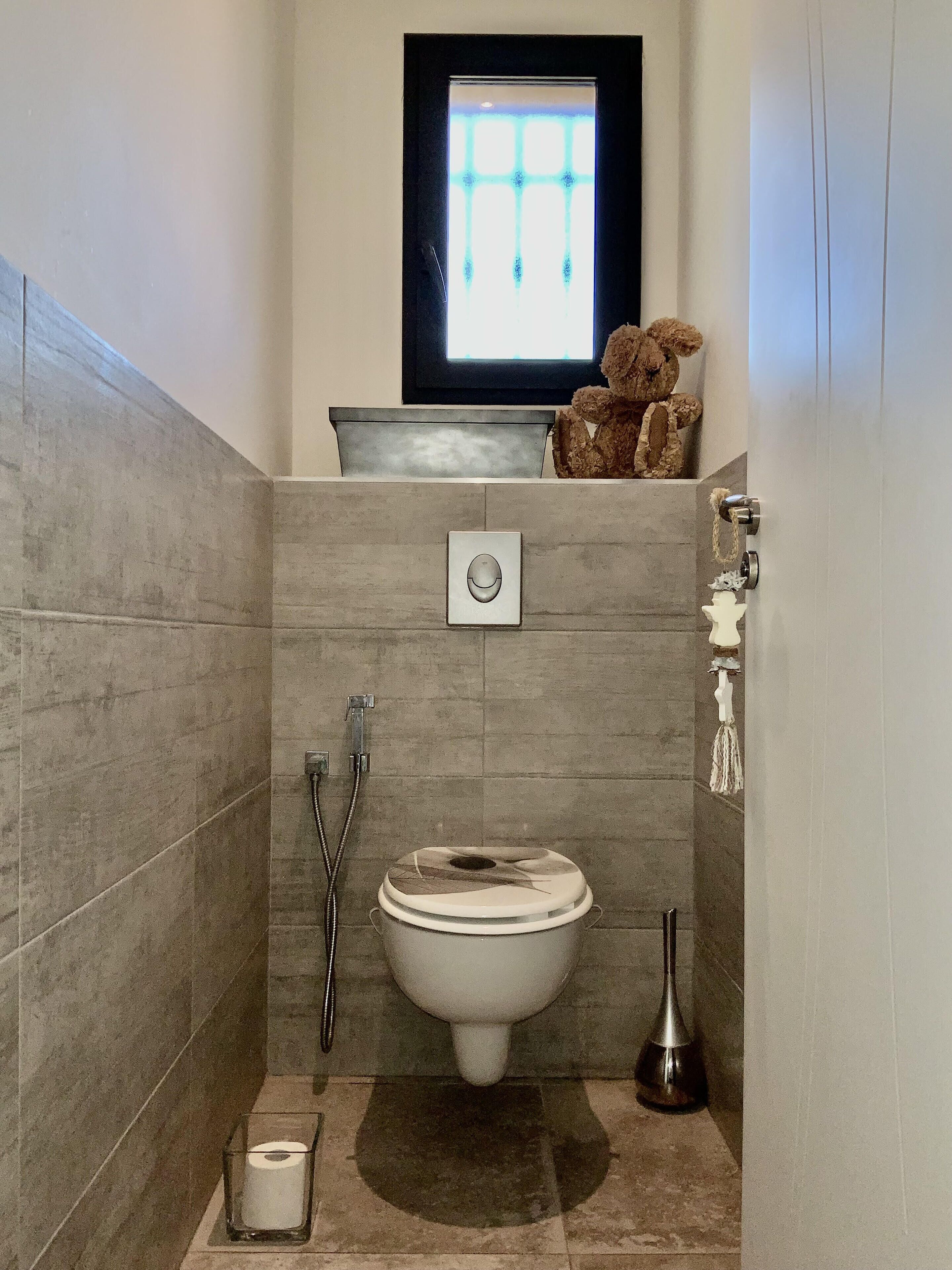 A small bathroom with a toilet, bidet, and a window above the sink.