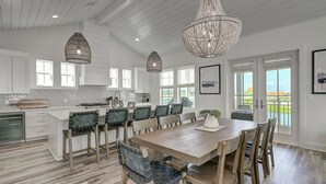 A spacious kitchen with white cabinetry, a large island, and a dining area with wooden chairs and a table.