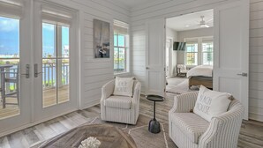 A spacious room with a large sliding glass door leading to a balcony, a bed with a TV, and two striped armchairs.