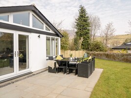 A modern house with a patio area featuring a dining table and chairs, a glass door entrance, and a view of a forested landscape.