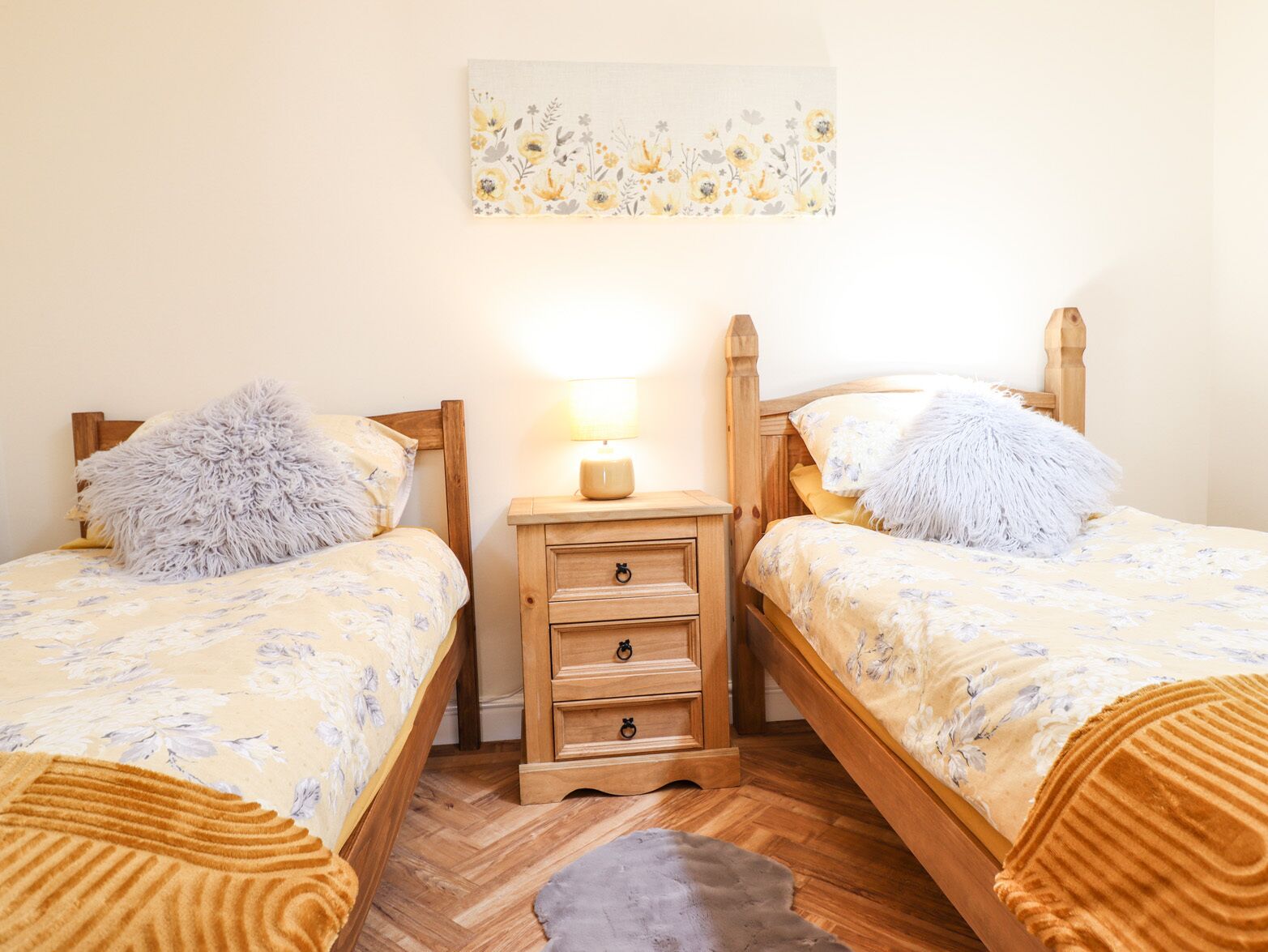 A bedroom with two wooden beds, a nightstand with a lamp, and a floral artwork on the wall.