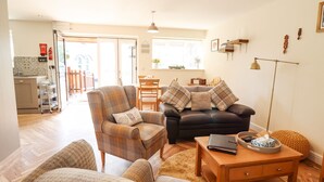 A living room with a sofa, armchairs, and a coffee table. There is a kitchen area with a refrigerator and a dining table. - Varley Villa (Newtown)