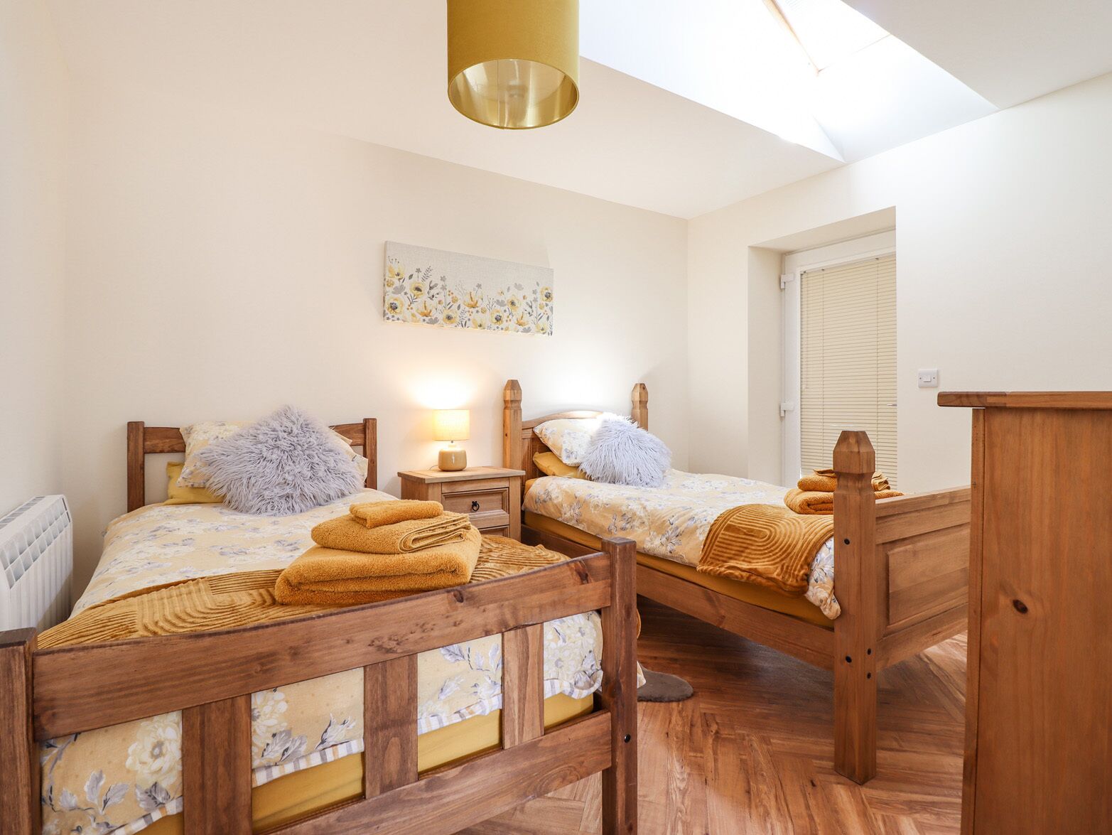 A bedroom with two wooden beds, a skylight, a radiator, and a painting on the wall.