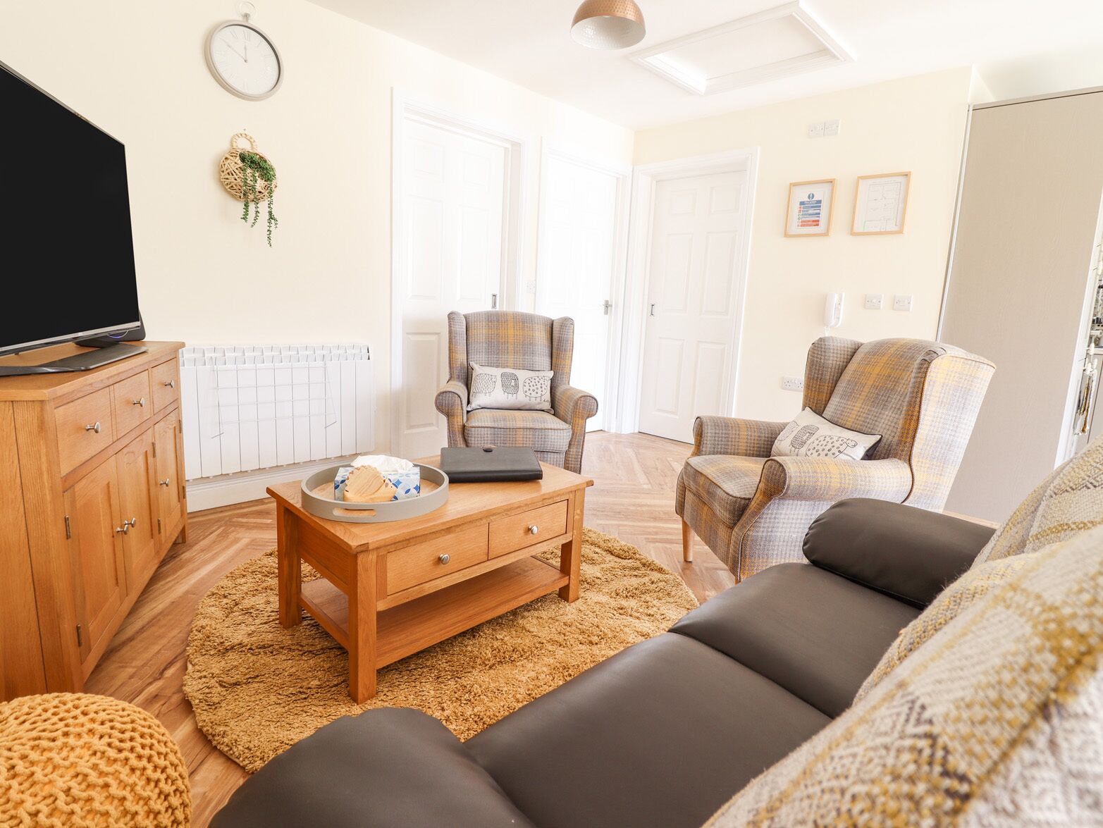 A living room with a sofa, armchairs, a coffee table, a television on a wooden cabinet, and a radiator.