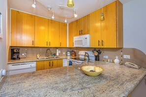 A kitchen with wooden cabinets, a microwave, a coffee maker, and a granite countertop. - Kamaole Sands #1-105 Renovated Ground Floor Unit, Partial Oceanview, A/C! (Kihei)