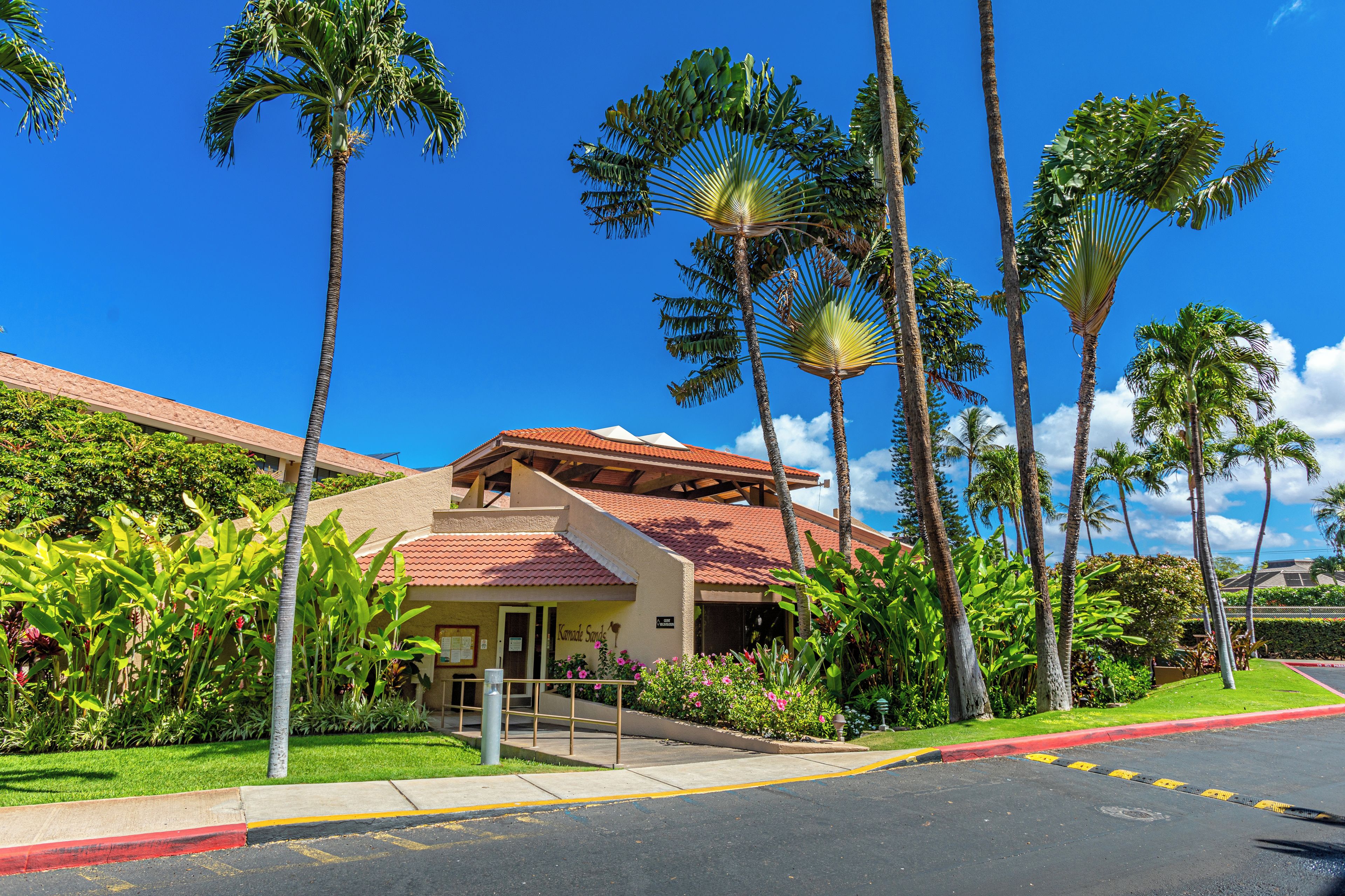 A hotel with a red-tiled roof, surrounded by palm trees and tropical plants.