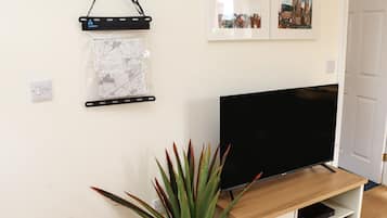 Una sala de estar con una televisión de pantalla plana sobre un soporte de madera, un mapa en la pared y una planta en maceta.