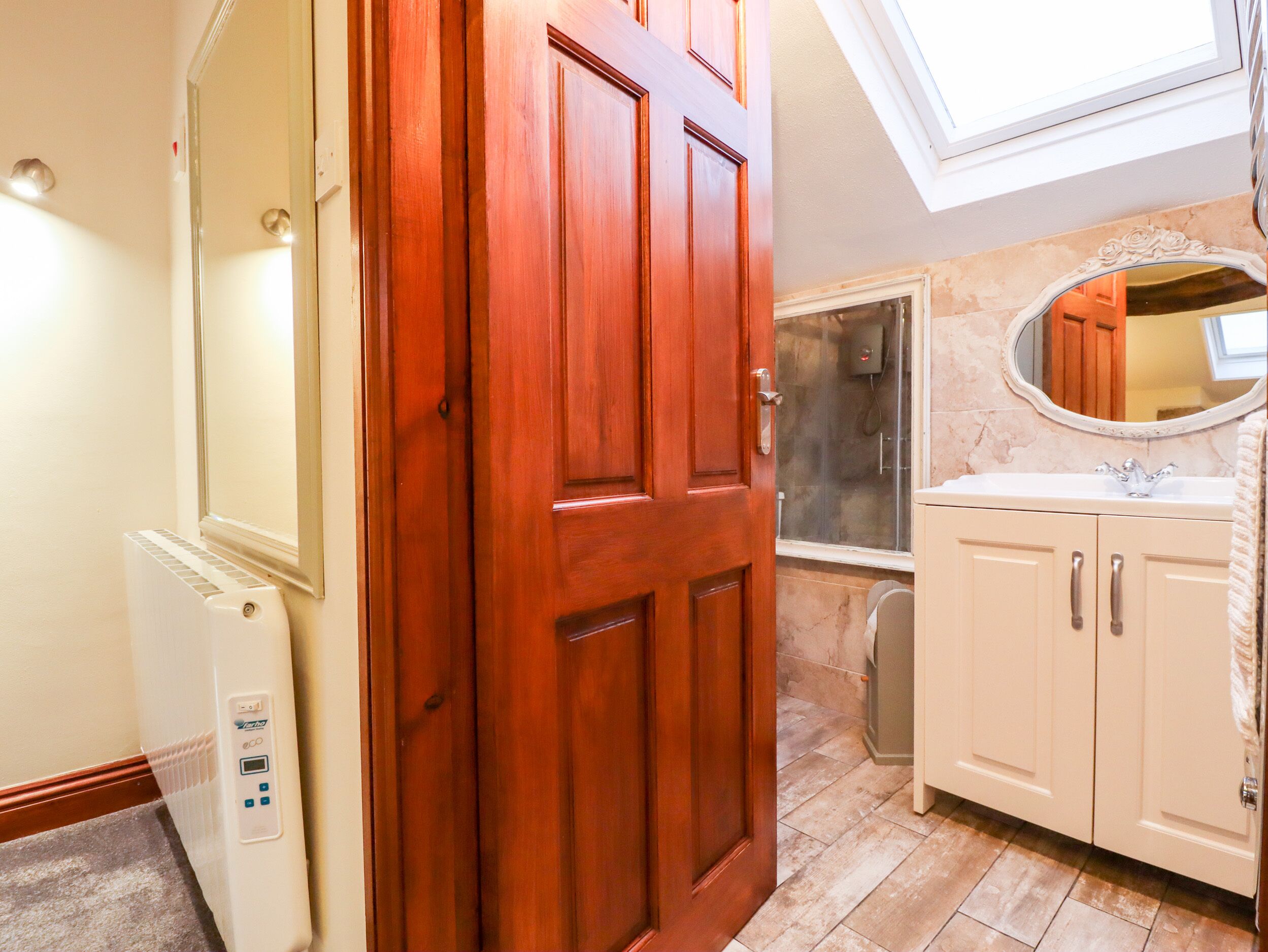 A bathroom with a wooden door, a white radiator, a shower, and a vanity with a mirror.