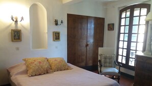 A bedroom with a bed, a chair, a wardrobe, and a window. - Typical Provencal village house with lovely terrace. (Riez)